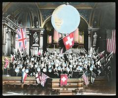 Interior of Zurich's Tonhall decorated for 1913 World's Sunday School Convention with a large globe, world flags, and convention members holding country banners