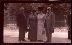 Four World Sunday School Association Convention delegates wearing pins and ribbons standing by cart and iron fence in 1913