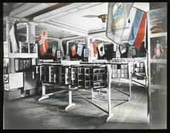 Literature exhibit at 1913 World's Sunday School Convention in Zurich featuring wooden stands with bible study materials and world flags