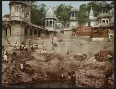Color photochrom print of Burning Ghat in Benares showing evening ritual with smoke and boats on the river