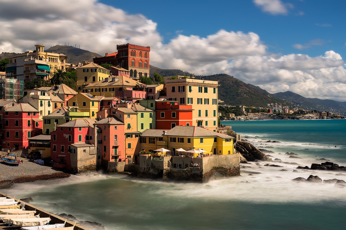 Colorful coastal town of Boccadasse in Genoa, Italy with red boats in the harbor and blue Mediterranean sea under warm sunlight
