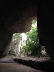 Ancient stone quarries Latomie dei Cappuccini in Siracusa with towering cliff walls and scattered greenery under clear sky