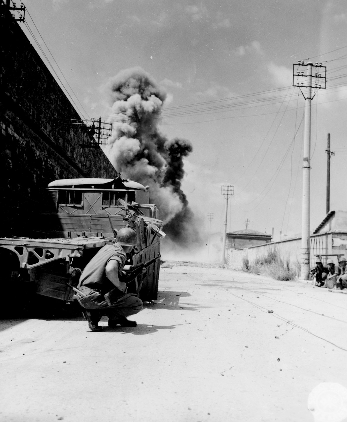 Soldier from 316th Engineer Combat Battalion alert for enemy snipers while comrades set off mines in street leading to Leghorn harbor, July 19, 1944
