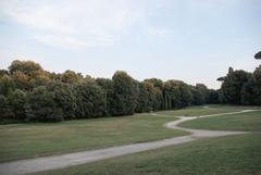 Trail path through meadow with green grass and scattered trees under a partly cloudy sky