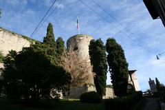 Rocca of Bergamo with ancient stone walls and greenery under a clear blue sky