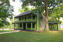 Large two-story historic home painted bright green with dark green trim and multistory porch