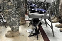 Soldiers and Marines standing for the pledge of allegiance during naturalization ceremony with flags placed on chairs
