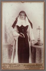 Portrait of Dymphna Gezelle (Sister Wilfina) standing with breviary next to table with crucifix