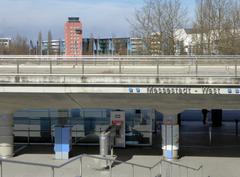 East entrance of the Messestadt West U-Bahn station in Munich under Willy-Brandt-Allee with old airport tower and trade fair grounds in background
