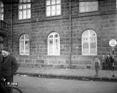Exterior view of the east side of Althingi, Icelandic parliament building with broken windows and youths standing by including one with a bicycle on March 31, 1949