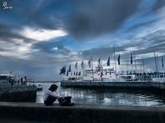 Child waiting alone at the wharf during evening blue hour with city skyline and pier in the background