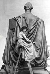 Elsie Ward Hering working on Seated Lincoln sculpture in chambray gown, dwarfed by the large statue
