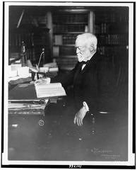 Andrew Carnegie seated at desk reading, three-quarter length portrait, facing left