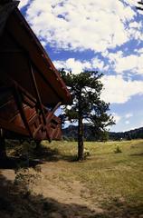 Mission 66 visitor center in Rocky Mountain National Park with surrounding plants and trees under a clear sky and mountains in the background