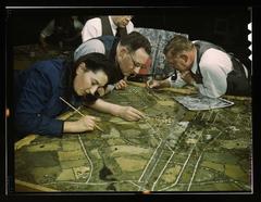 Camouflage class at New York University in 1940s with men and women preparing military and industrial camouflage models using aerial photographs