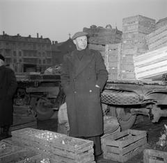 Mr. Dirchsen standing next to auction crates filled with onions and trucks loaded with vegetables including potatoes in the background on a farm in Denmark
