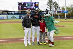Rear Admiral Joe Cahill posing with Norfolk Tides player Connor Pavolony and mascot Triton after ceremonial first pitch at Norfolk Tides baseball game