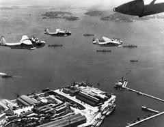 U.S. Navy Martin PBM-3S Mariner patrol bomber flying over Brazilian naval dockyard at Rio de Janeiro with incomplete destroyers visible, December 1943