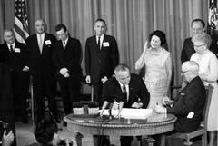 President Lyndon B. Johnson signing Medicare Bill at Harry S. Truman Library with dignitaries in black and white