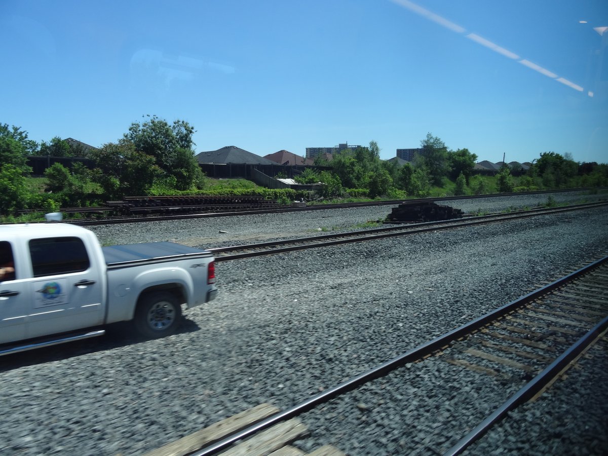 View through train window showing urban landscape with trees and railway tracks heading towards Pearson Airport
