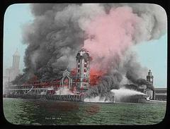 Fireboats fighting a large fire at Seattle's Grand Trunk Pacific Dock on July 30, 1914, with smoke billowing over the waterfront and nearby buildings including Smith Tower