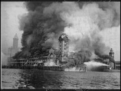 Fire at Seattle's Grand Trunk Pacific Dock on July 30, 1914 with fireboat Duwamish combating flames and smoke near Colman Dock clock tower