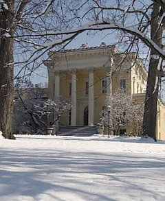 Snow-covered Italian-style gardens and evergreen trees surrounding the columned front of a historic Baltimore mansion