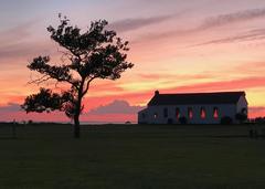 Chapel and tree silhouetted against a vibrant pink sky at sunset
