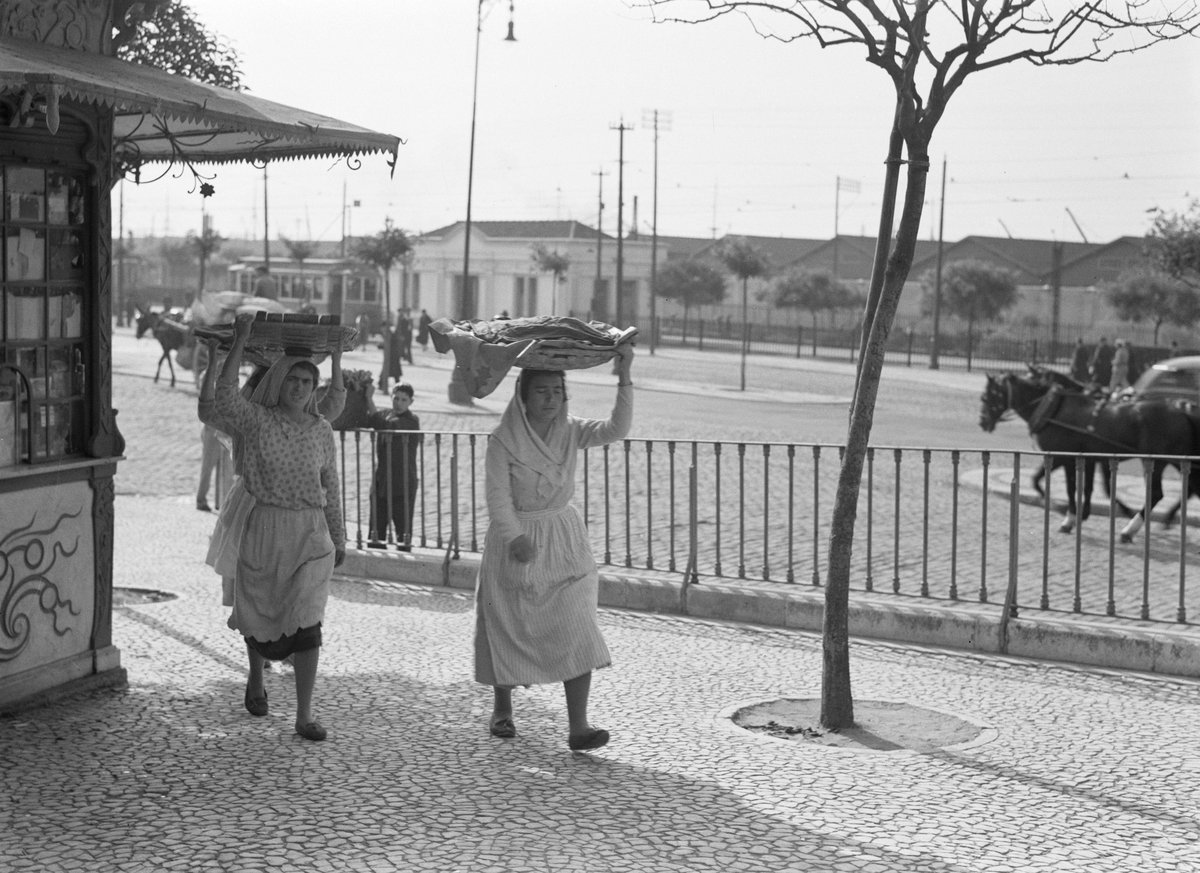 Women carrying baskets on their heads next to a kiosk in Lisbon, Portugal, May 1935