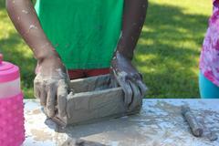 Hands covered in clay shaping a brick in mold during brick making activity