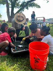 Park ranger teaching four smiling children archaeology digging using brushes and tools