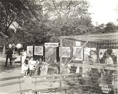 Children viewing sculptures and hanging artworks labeled Henry St. settlement outdoors near a monkey cage
