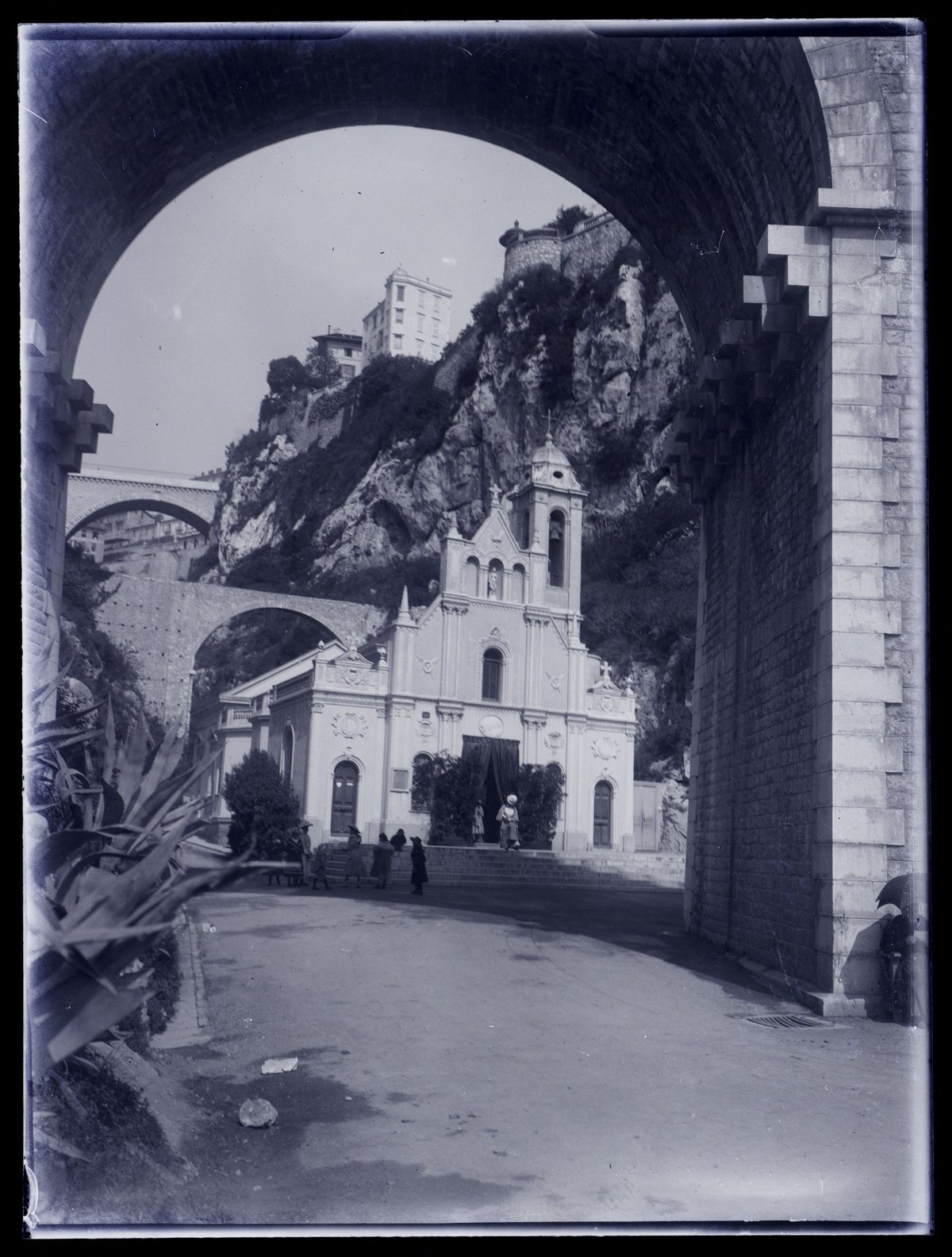Viaduct arch and bell tower of Sainte-Dévote Church with rocky slope and street in Monaco in 1906