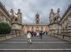 Visitors climbing the marble steps of the Cordonata at Capitoline Museums entrance in Rome with statues of Castor and Pollux and Palazzo Senatorio clock tower
