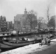 Historic scene of inner ships in Amsterdam canal with bakfiets carrying milk bottles and Noorderkerk church in background