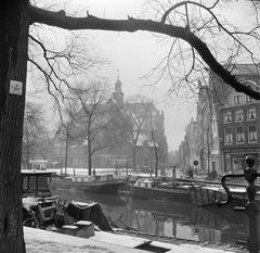 Boats in Amsterdam canal with Noorderkerk church in background during winter, January 1955