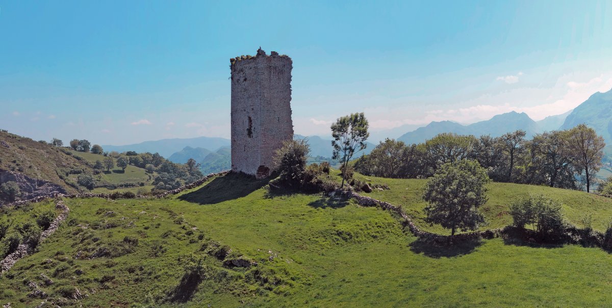 View of Torreón de Peñerudes, an ancient stone tower surrounded by green trees under a clear sky