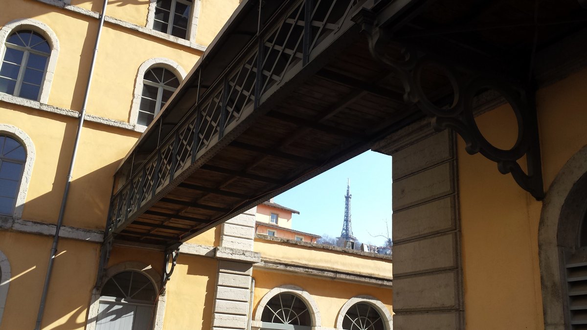 View of the metal tower of Fourvière in Lyon from behind the Subsistances buildings with a wooden and metal footbridge in the foreground