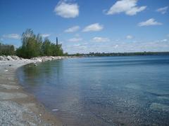 View of Leslie Street Spit peninsula extending into Lake Ontario with green vegetation and urban skyline in the background
