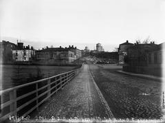 Historic black and white photo of Vuorimiehenkatu street with buildings 7, 9, 11 and Tähtitorninkatu 10 behind Ullanpuistikko park in Helsinki, water post at corner, observatory of the University of Helsinki on Tähtitorninvuori hill in background