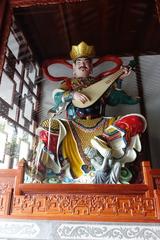 Eastern Dhṛtarāṣṭra statue at the Temple of the Six Banyan Trees wearing white clothes and armor holding a pipa