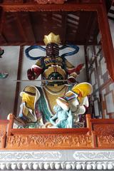 Southern Virūḍhaka statue at the Temple of the Six Banyan Trees wearing blue clothes and holding a sword