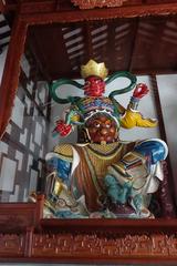 The western Virūpākṣa statue at the Temple of the Six Banyan Trees wearing red clothes with a dragon or snake wrapped around arm