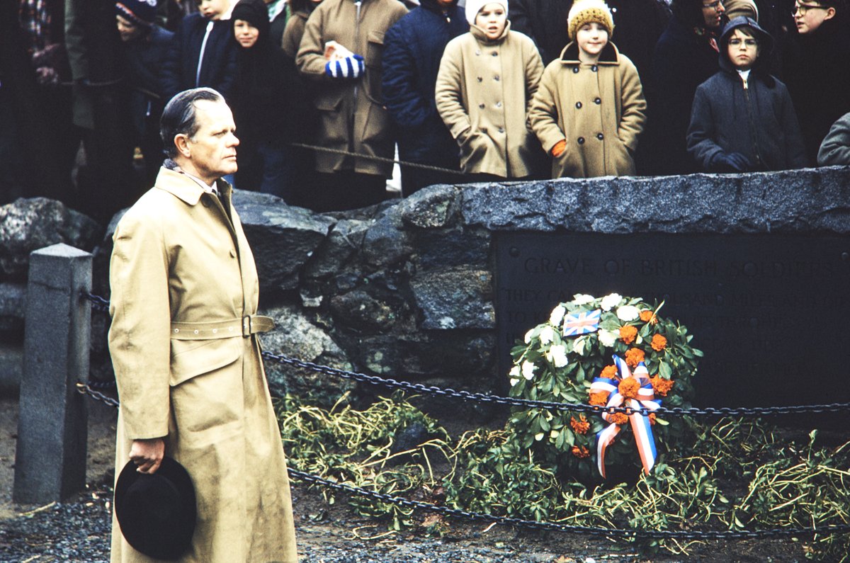 Visitor standing at a monument dedicated to British soldiers killed in the Concord Fight, surrounded by trees and plants in Minute Man National Historical Park