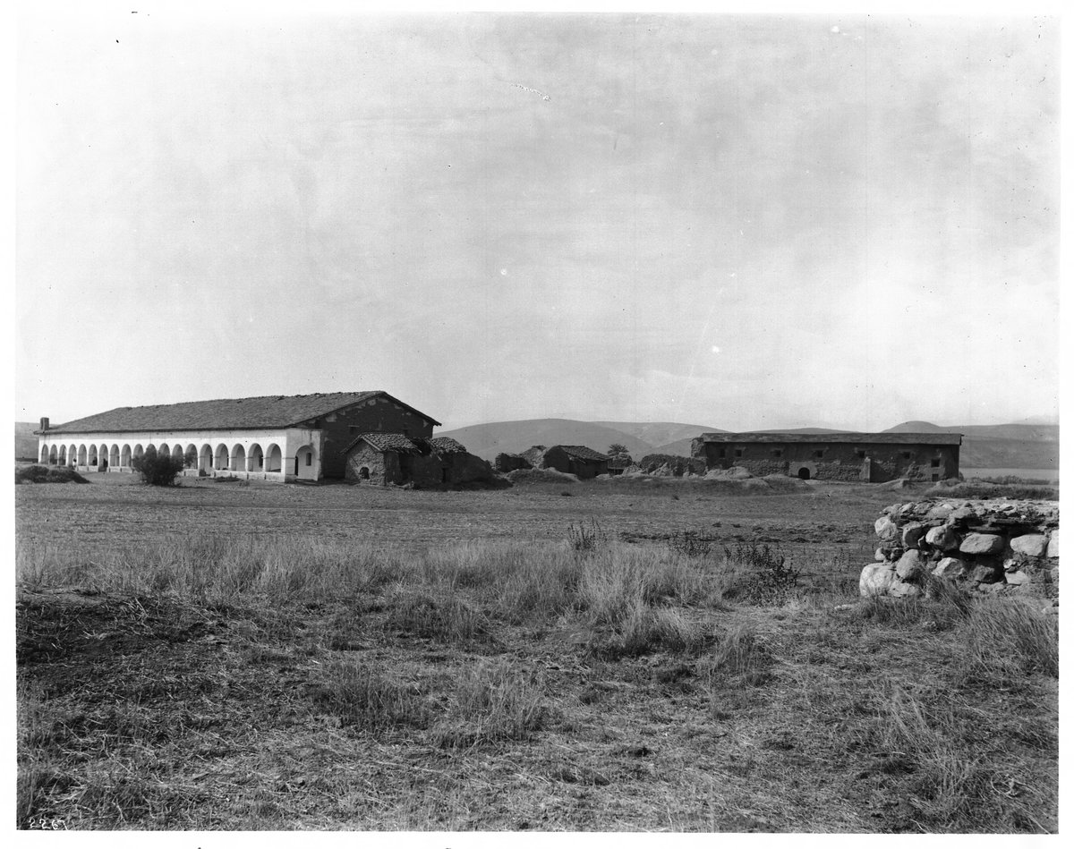Historic view of Mission San Fernando Rey de España from the southeast with arches and nearby buildings in disrepair in San Fernando Valley, 1904