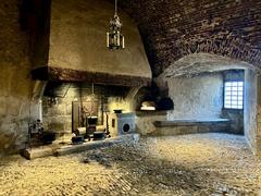 Interior view of the kitchen in Château de Gruyères with rustic stone walls and historical cooking equipment