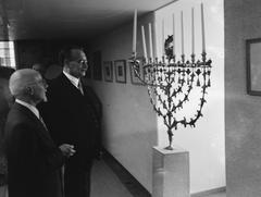 Dr. W. Drees and E.A. Rodrigues Pereira standing next to a menorah at the reopening of the Jewish Historical Museum in the Waaggebouw