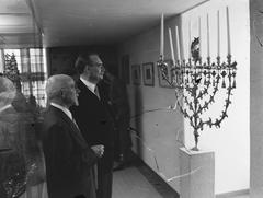 Dr. W. Drees standing beside a menora in the Waaggebouw during the reopening of the Jewish Historical Museum in 1955