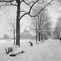 Snow-covered bench in Hofgarten park with Bavarian State Chancellery building in background in Munich winter
