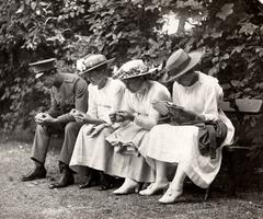 Three young women in white clothing and hats sitting on a bench with a young man in uniform at Artis zoo in Amsterdam, 1917